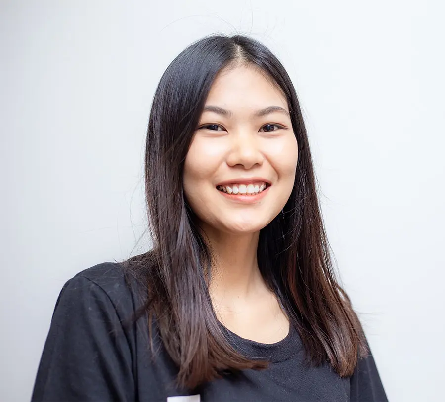 Young woman with long dark hair smiling warmly against a plain white background, wearing a black shirt. Conveys a positive and friendly tone.