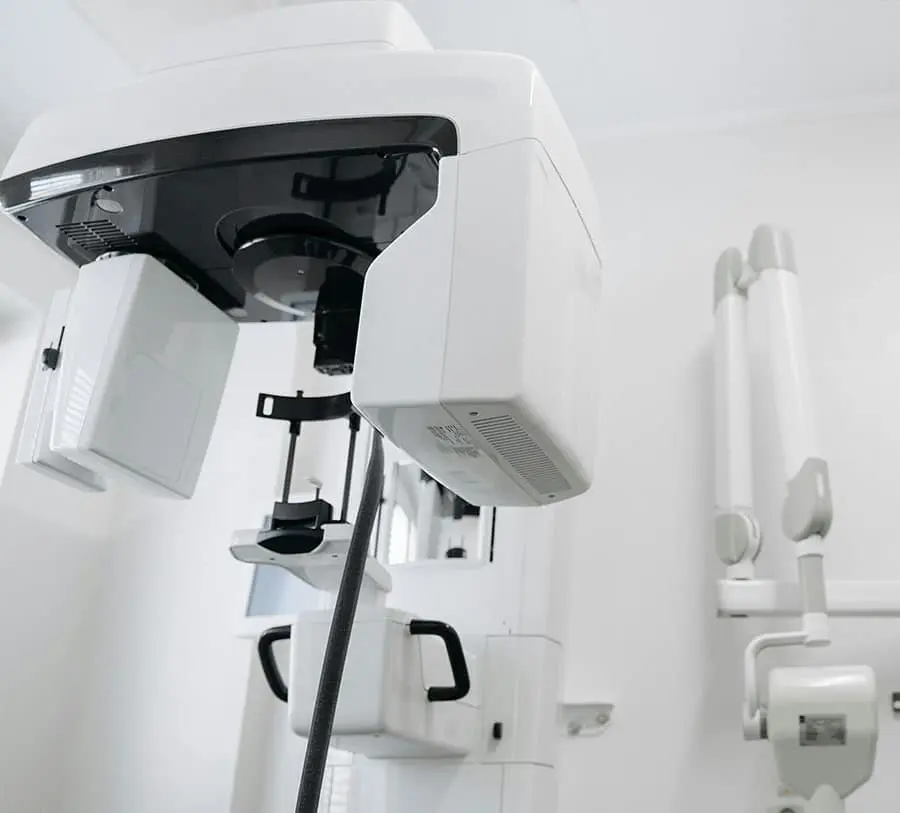White dental panoramic X-ray machine in a clean clinic. The device has a sleek, modern design, creating a clinical and professional atmosphere.